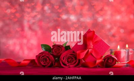 Rose rosse e da regalo in velluto rosso tessuto. Candele rosse con bokeh di luce sullo sfondo cuori Foto Stock