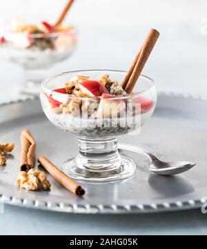 Una vista ravvicinata di un vetro piatto di acciaio tagliati avena mescolati con semi di Chia e di sementi di canapa e guarnita con dadolata di mele, noci e bastoncini di cannella. Foto Stock