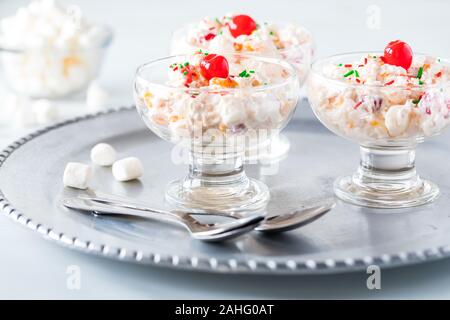 Fronte di un vista ravvicinata di tre piatti di vetro riempito con Ambrosia insalata e guarnita con ciliegie al maraschino su un vassoio di metallo Foto Stock