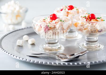 Una chiusura in vetro piatti da dessert riempito con insalata di ambrosia e rabboccato con ciliegie al maraschino e una piccola ciotola di mini marshmallows. Foto Stock