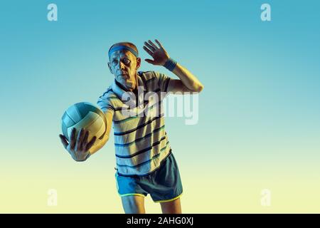 Senior uomo che indossa sportwear giocando a pallavolo sul gradiente dello sfondo, una luce al neon. Caucasica modello maschile in grande forma rimane attivo. Concetto di sport, attività, movimento, benessere e fiducia. Foto Stock