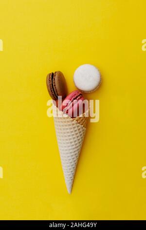 Macarons dolci. Stil life foto del cono di cialda con amaretti su sfondo giallo. Lay piatto, dessert cibo. Foto Stock