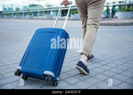 Uomo elegante a piedi per l'aeroporto con valigia blu. Uomo d'affari in viaggio. Foto Stock