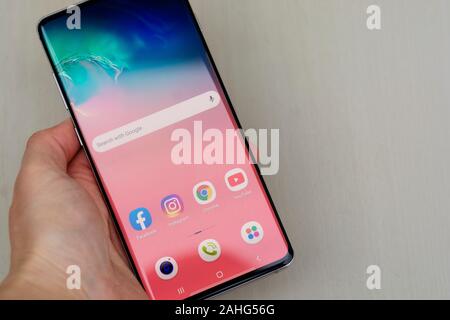 Corby, Regno Unito. Dicembre 25, 2019 - Samsung Galaxy S10 telefono cellulare, mano azienda S10 di bianco su sfondo blu. Editoriale illustrativa Foto Stock