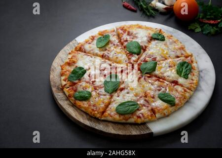 Una deliziosa pizza su sfondo scuro, vista dall'alto. Artiginale piza rotondo con il formaggio su sfondo scuro. Foto Stock