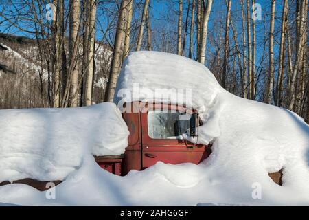 Un vecchio camion rosso sepolto nella neve in una giornata di sole nella foresta di Alaskan Foto Stock