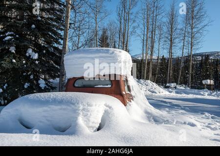 Un vecchio camion rosso sepolto nella neve in una giornata di sole nella foresta di Alaskan Foto Stock