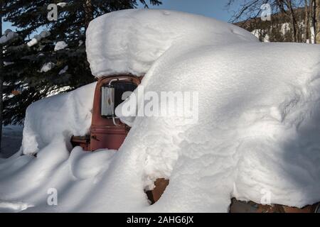 Un vecchio camion rosso sepolto nella neve in una giornata di sole nella foresta di Alaskan Foto Stock