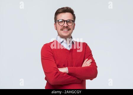Uomo in felpa rossa e i bicchieri in piedi nella parte anteriore della fotocamera, sentimento positivo e fiducioso Foto Stock