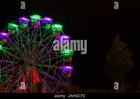 Ruota grande con luci al neon colorate in inverno Natale notte a San Sebastian, Paesi Baschi. Concetto di attrazione per il divertimento all'aperto Foto Stock