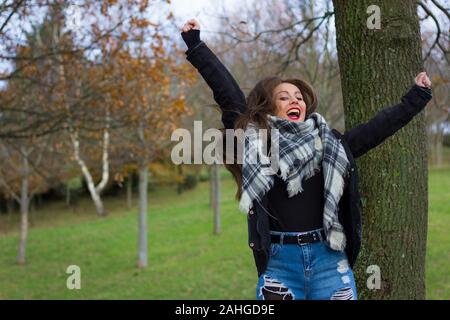 Oltre eccitato giovane donna salta in aria con le braccia in alto nella stagione autunnale la giornata al parco. Studente di College exam pass-NOZIONE Foto Stock