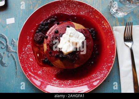 Una targhetta rossa di una pila di pancake con lamponi mirtilli e yogurt in una caffetteria locale Foto Stock