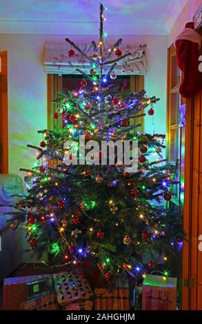 Albero di Natale decorato con baubles, tinsel e le luci di Natale con regali di Natale intorno alla base, Surrey, England, Regno Unito Foto Stock