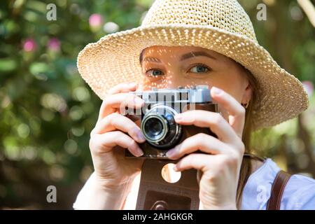 Primo piano ritratto di una bella donna in paglia cappello di viaggio nella foresta tropicale, scattare foto su retro fotocamera. Illumina le ombre attraverso dettagli ritagliati Foto Stock