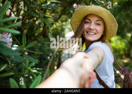 Bella donna in cappello di paglia viaggio nella foresta tropicale, camminando lungo il sentiero di legno, che conduce il suo partner. Turistico con zaino. Seguimi il concetto. Foto Stock