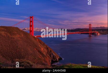 Panorama del Golden Gate bridge al tramonto con il Marin Headlands in primo piano lo skyline di San Francisco e le nuvole colorate in background Foto Stock