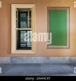 Bellissima ed elegante rettangolare cornice verde ornato di confine e finestra stretta con la chiusura dell'otturatore verde sulla parete arancione con pavimento di marmo bianco, abbandonata nel vecchio edificio Foto Stock