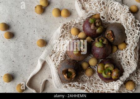 Piano di composizione dei laici con fresco mangosteen mature e frutti longan in stringa male su sfondo della carta. Rifiuti Zero shopping libero in plastica concetto. Foto Stock