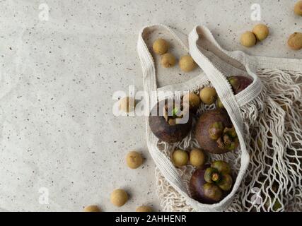 Piano di composizione dei laici con fresco mangosteen mature e frutti longan in stringa male su sfondo della carta. Rifiuti Zero shopping libero in plastica concetto. Foto Stock