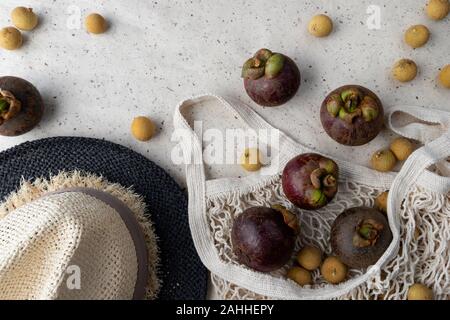 Piano di composizione dei laici con fresco mangosteen mature e frutti longan in stringa male su sfondo della carta. Rifiuti Zero shopping libero in plastica concetto. Foto Stock