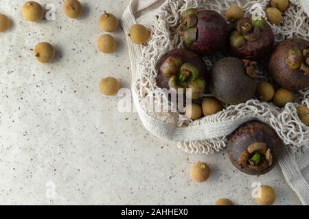 Piano di composizione dei laici con fresco mangosteen mature e frutti longan in stringa male su sfondo della carta. Rifiuti Zero shopping libero in plastica concetto. Foto Stock