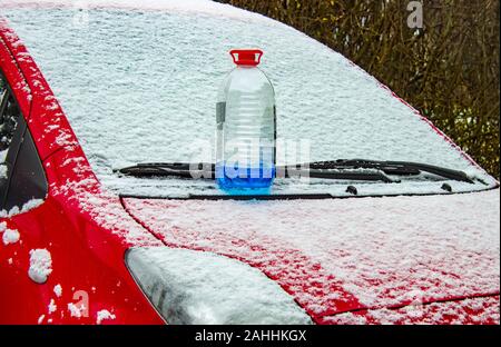 Antigelo per lavacristalli sorge sulla parte anteriore del cofano di auto rossa nella neve in inverno. Foto Stock