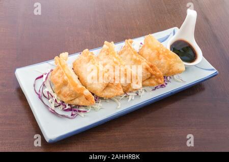 Gyoza e taluni vegetali servite con salsa di shoyu sulla piastra giapponese sul tavolo di legno Foto Stock