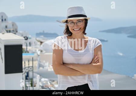 Fiducioso donna sorridente turista in viaggio sulla crociera di lusso nel Mediterraneo, Grecia, Santorini. Femmina con bracci ripiegati guardando la telecamera, sfondo Foto Stock