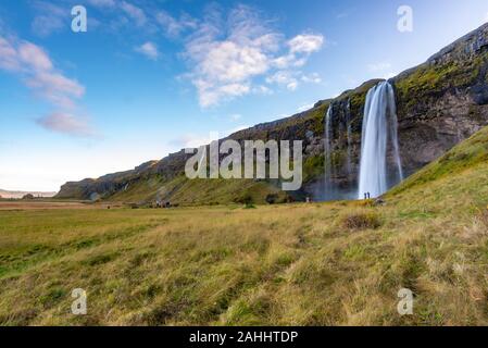 Cascata Seljalandfoss visto da lontano con un irriconoscibile visitatori, prese con un cielo chiaro alla fine di un inizio di ottobre pomeriggio, Islanda Foto Stock