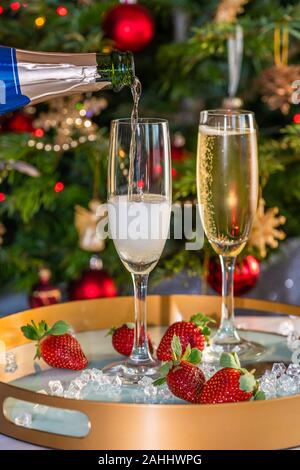 Champagne versato in bicchieri con le fragole su sfondo di festa Foto Stock