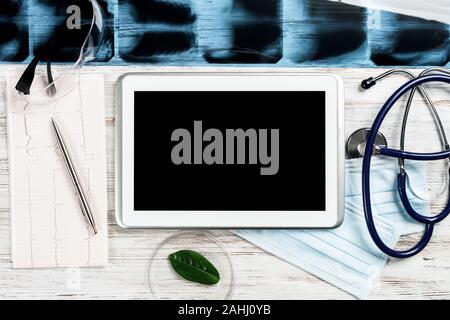 Risultato di laboratorio di esame paziente giace sul piano medico. Vista superiore tablet Pc con schermo vuoto, immagine a raggi x, uno stetoscopio e cardiogram su Foto Stock