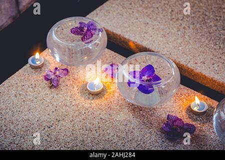 Fiori viola sulla vaschetta piena di acqua con poco candela sul terreno Foto Stock