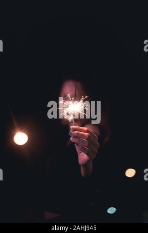 Signora azienda botti stick sul fuoco per chiudere il suo volto in avanti a outdoor con luce bokeh di fondo della lampadina della luce di notte Foto Stock