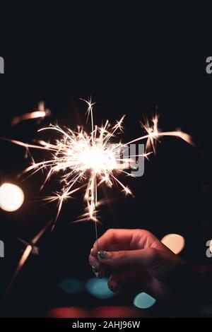 Donna di mano azienda botti stick sul fuoco grande diffusione della fiamma lungo la luce con bokeh di fondo della lampadina della luce di notte tempo su sfondo nero Foto Stock