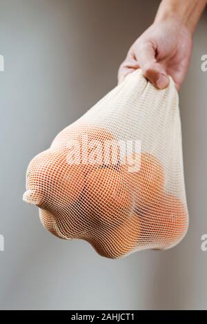 Primo piano di un uomo con un tessile riutilizzabile borsa a rete, utilizzato per acquistare generi alimentari alla rinfusa, pieno di arance, come misura per ridurre l'inquinamento in plastica Foto Stock