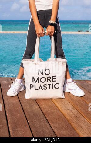 Ragazza giovane azienda eco cotone sacco con segno non più in plastica blu sul mare tropicale sfondo Foto Stock