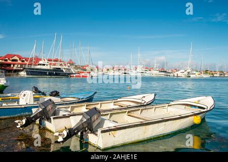 Vecchio e semplice la pesca barche e yacht di lusso e barche in background nella soleggiata giornata estiva a marina di Eden Island, Mahe, Seicelle Foto Stock