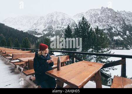 Donna con una bevanda calda da thermos Cup che si affaccia nevato Alti Tatra picchi Foto Stock