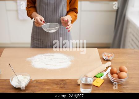 Elevato angolo di visione di un irriconoscibile donna setacciatura di lievito in polvere durante le riprese di un tutorial di cottura in cucina, spazio di copia Foto Stock