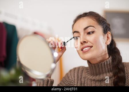 Ritratto di sorridente giovane donna applicando il mascara alle ciglia mentre si fa fare fino a casa, spazio di copia Foto Stock
