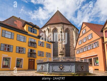 Dinkelsbuhl, Germania - 11 Maggio 2019: Lowenbrunnen (Lion Fontana) molla con Lion statua sulla sommità di un pilastro a Altrathausplatz con San Giorgio min. Foto Stock