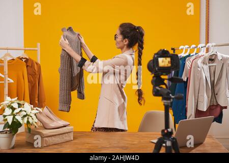 Ritratto di giovane contemporanea donna azienda maglione maglia durante le riprese del video per la moda e bellezza canale contro sfondo giallo, spazio di copia Foto Stock