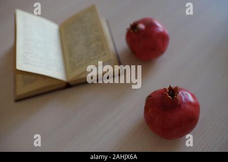 Due interi mature melograno e aprire un libro di ricette sulla luce di un tavolo di legno. Foto Stock