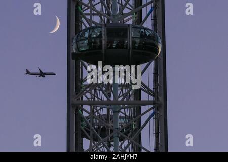 Westminster, Londra, 30 dic 2019. Un aereo passato il London Eye cabine, con la luna visibile accanto al punto di riferimento. Un splendidamente soleggiata giornata invernale a Londra si conclude con un delicato pastello tramonto a Westminster. Credito: Imageplotter/Alamy Live News Foto Stock