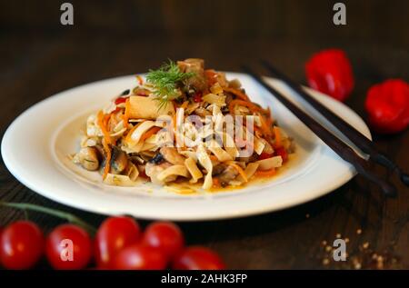 Tagliatelle con insalata di gamberetti su una piastra bianca e bastoni. Il coreano piccante-insalata di stile su di un tavolo di legno. Foto Stock