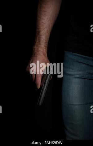 Un uomo con una pistola in mano su uno sfondo nero. Killer con una pistola Foto Stock