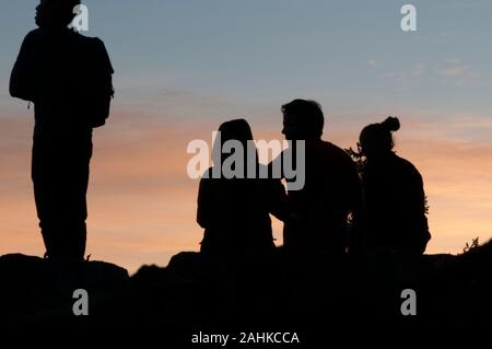 Quattro persone stagliano e guardare il tramonto Foto Stock