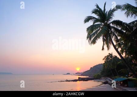 Un Tropical Bay con un mare calmo e palme, bagliore rosso dal sole al tramonto sulla spiaggia Viaguinim, Panaji, Goa, India, formato orizzontale Foto Stock