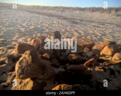 Sunrise sulle stoviglie rosse falò sulla spiaggia con un cerchio di pietre Foto Stock