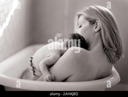 Vista laterale di una donna in una vasca da bagno mentre tiene il suo bambino. Foto Stock